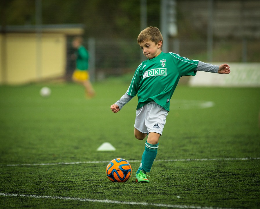 En kille i grön tröja sparkar på en fotboll.