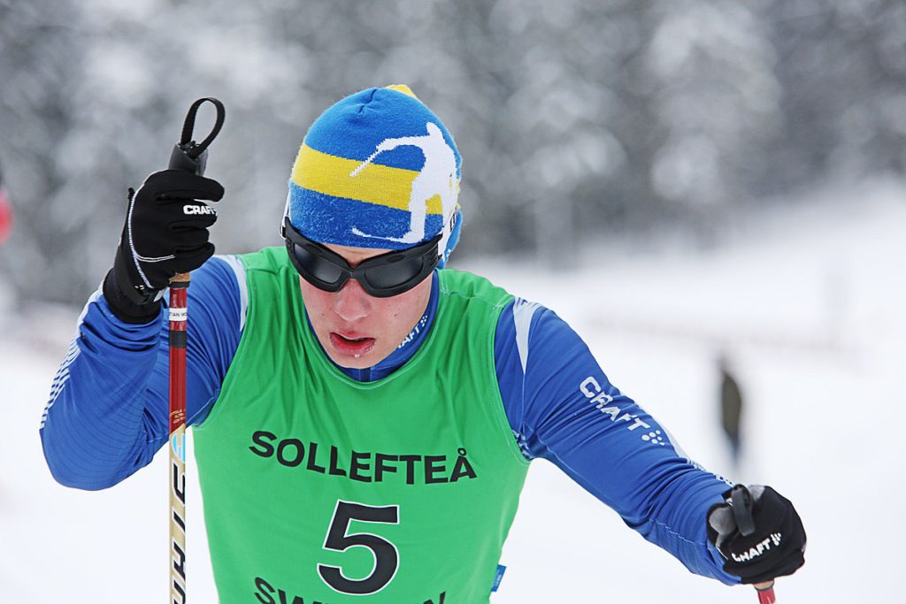 Zebastian Modin kämpar på sina skidor. Han har ett par svarta, mörkläggande glasögon för att alla ska tävla på samma villkor.